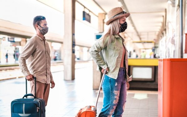 shows people wearing masks and queuing at a safe distance in a train station